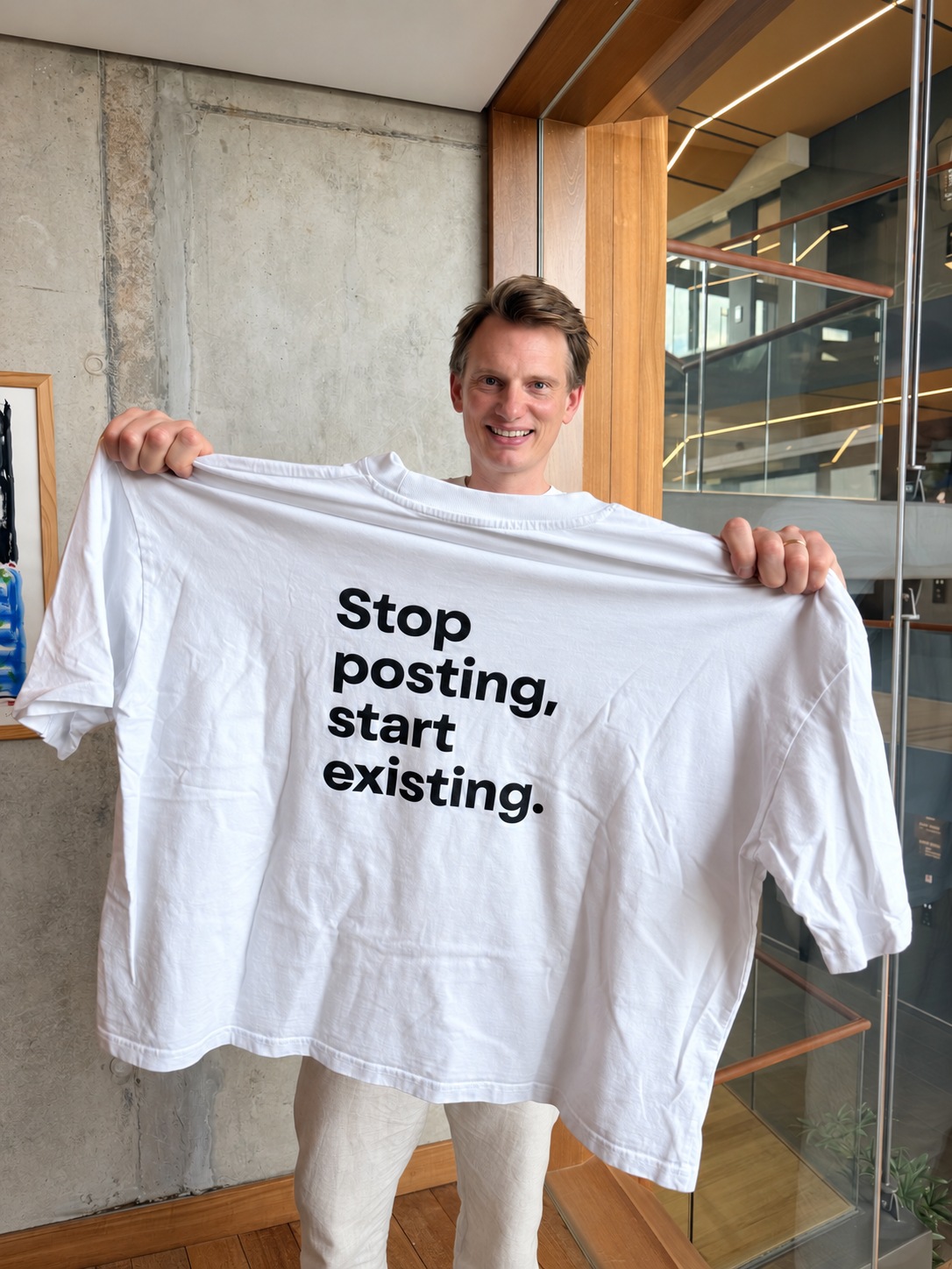 Homme souriant tenant un grand t-shirt blanc imprimé dans un bureau de verre et de bois